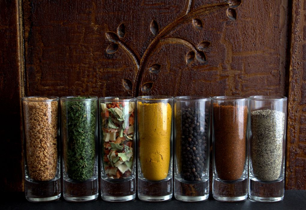 Colourful spices in glasses against a dark antique cabinet.